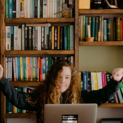 young girl celebrating while learning at her laptop
