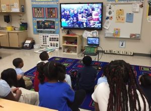 kids in a classroom watching a tele-conference lesson
