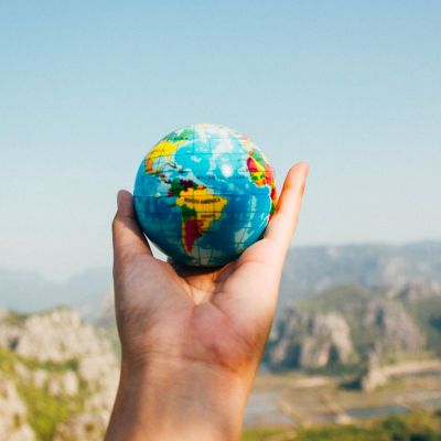 Hand holding a small globe with mountain scenery behind