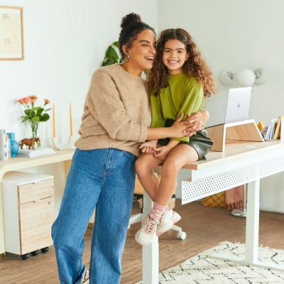 young girl sitting on a desk and woman hugging her