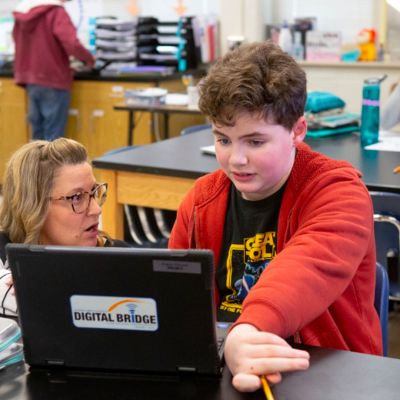 Teacher helping a student at a laptop