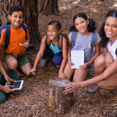 Students and teacher crouching under a tree.