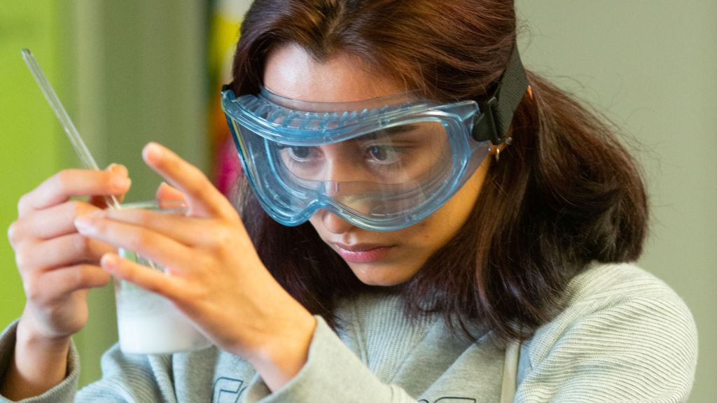 A high school girl mixes chemicals during a chemistry experiment.