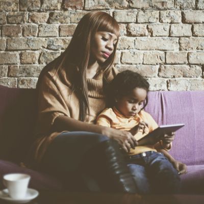 Mother and child reading a book, sitting on a couch.