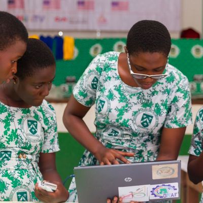 A teacher and students working together on a laptop.