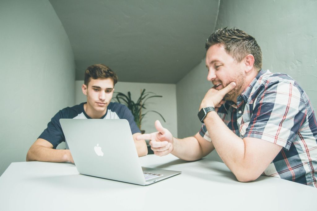 Two people talking, while looking at a laptop.