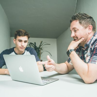 Two people talking, while looking at a laptop.