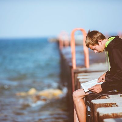 Boy sitting on a dock with a book.