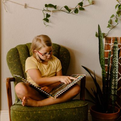 Girl sitting in a chair, reading a book.