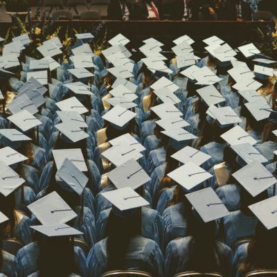 People in graduation outfits, sitting down and waiting.
