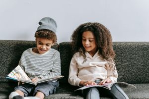 two kids reading books together on couch