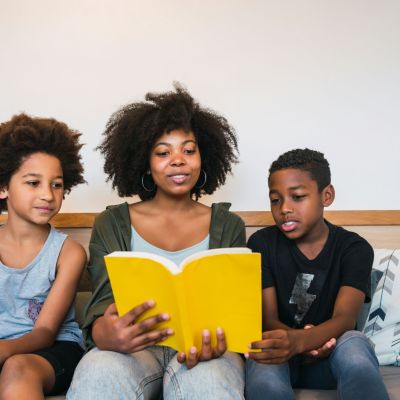 A parent reading a book to two children.