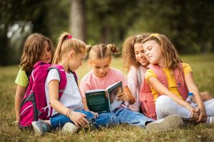 Children sitting in the grass reading a book.