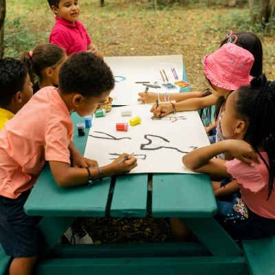 Children sitting together, working on artwork, and a picnic table.