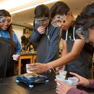 Three high school boys and one high school girl work together on an experiment in AP chemistry class.